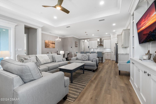 living room with ceiling fan with notable chandelier, a raised ceiling, hardwood / wood-style flooring, and crown molding