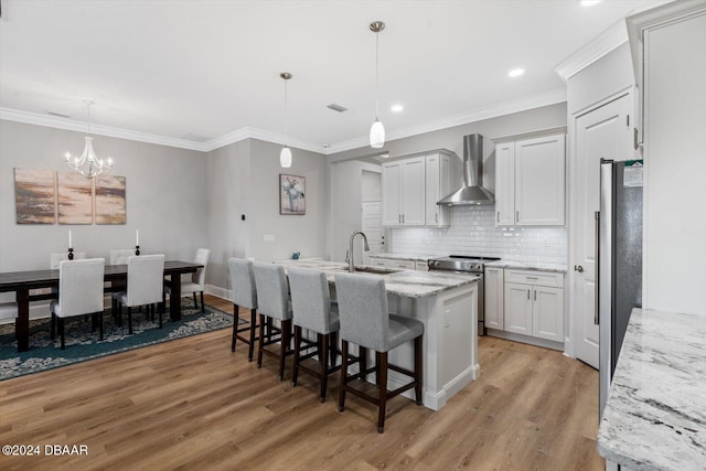 kitchen with stainless steel appliances, light wood-type flooring, wall chimney range hood, light stone countertops, and white cabinets