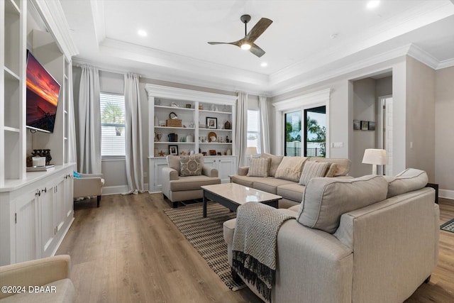 living room featuring light wood-type flooring, ceiling fan, crown molding, and a raised ceiling