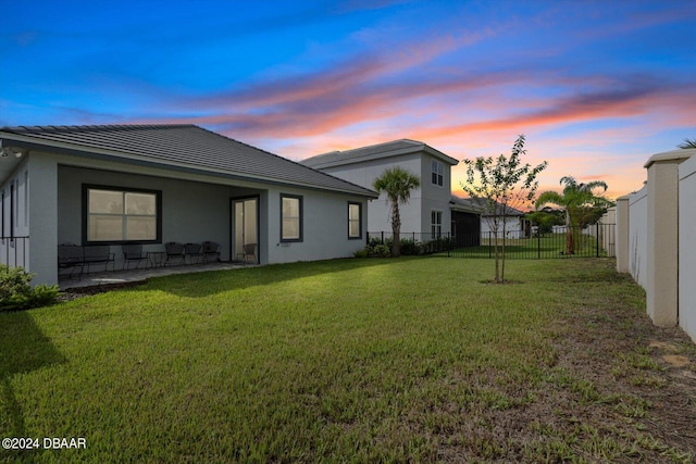 back house at dusk featuring a patio and a yard