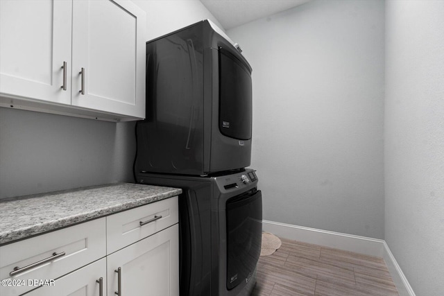 clothes washing area with stacked washer / drying machine and cabinets