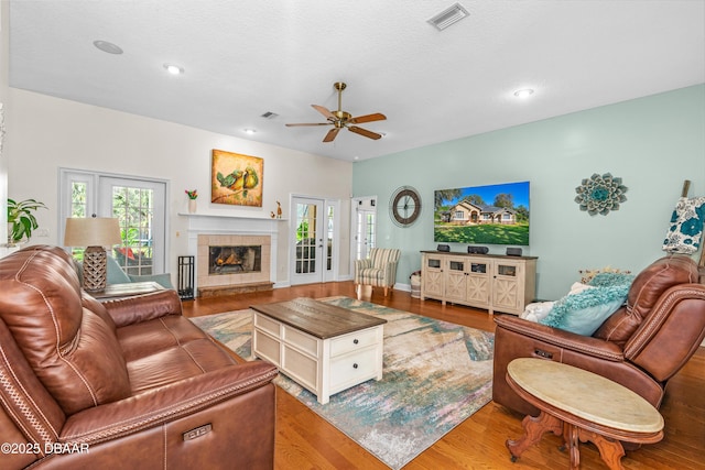 living room with visible vents, wood finished floors, ceiling fan, and a tiled fireplace