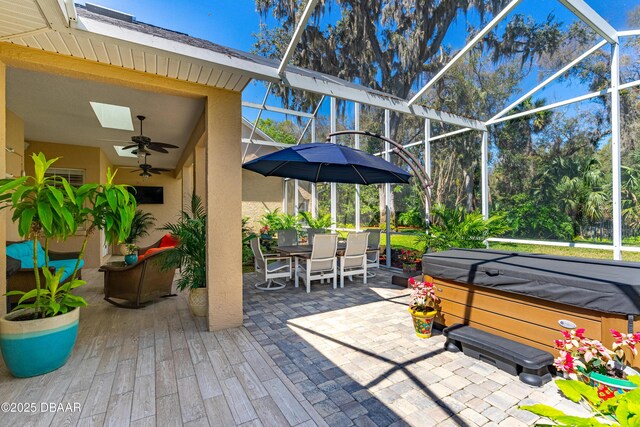 view of patio / terrace with outdoor dining space, glass enclosure, ceiling fan, and a hot tub