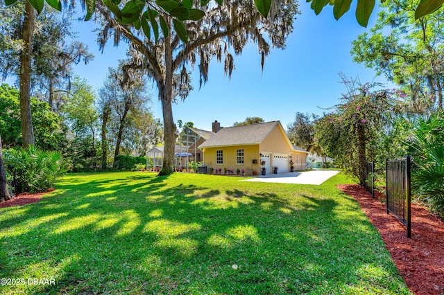 view of yard featuring concrete driveway, central AC unit, fence, and a garage