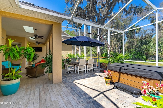 view of patio / terrace with outdoor dining space, glass enclosure, a ceiling fan, and a hot tub