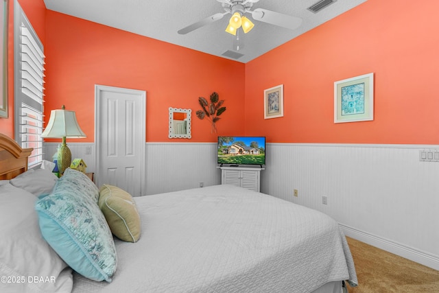 bedroom with a wainscoted wall, visible vents, a ceiling fan, a closet, and carpet