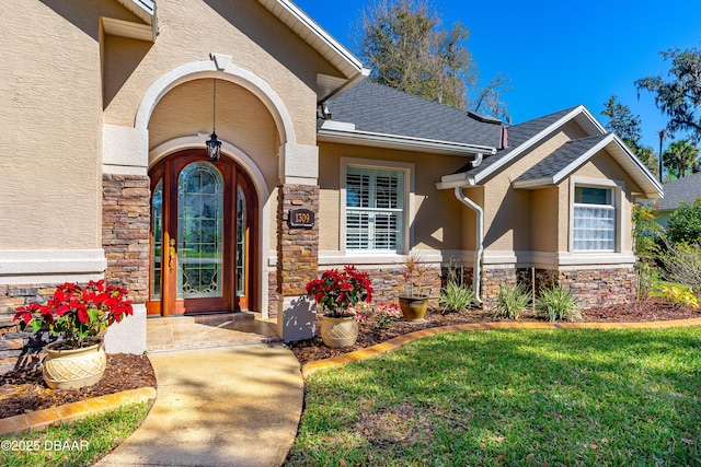 property entrance with stone siding, stucco siding, a lawn, and a shingled roof