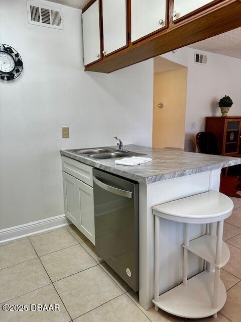 kitchen with sink, light tile patterned floors, stainless steel dishwasher, kitchen peninsula, and white cabinets