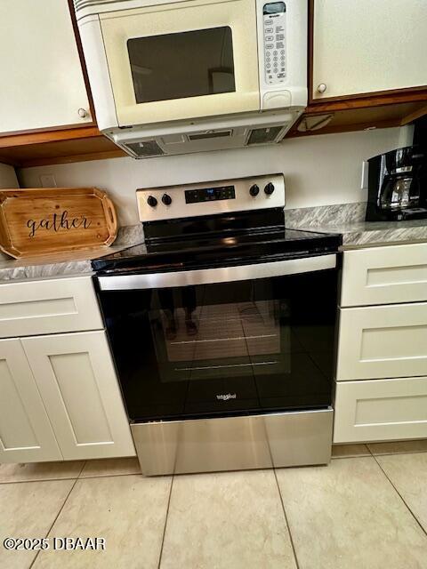 kitchen featuring light tile patterned floors, white cabinets, and stainless steel range with electric stovetop