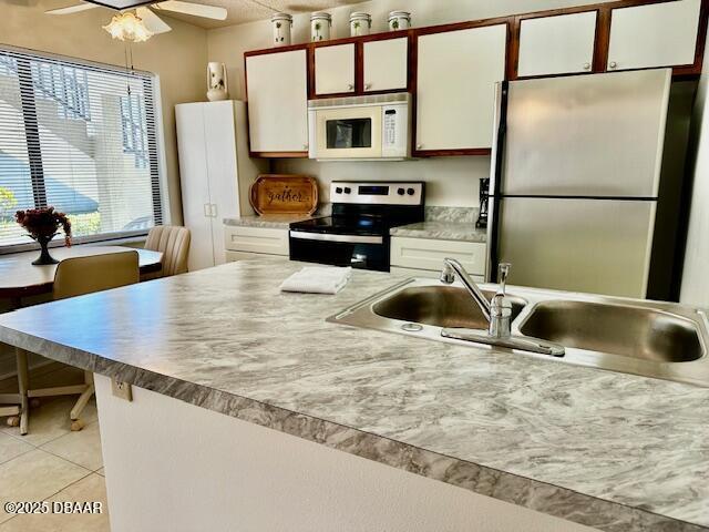 kitchen with sink, light tile patterned floors, ceiling fan, appliances with stainless steel finishes, and white cabinetry