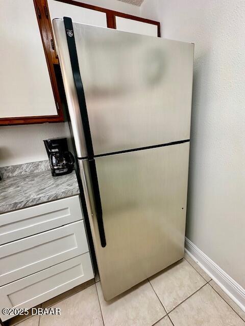 kitchen featuring stainless steel refrigerator, white cabinetry, and light tile patterned floors