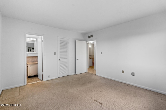 unfurnished bedroom featuring light colored carpet, visible vents, ensuite bath, and baseboards