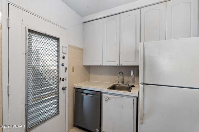 kitchen with light countertops, stainless steel dishwasher, freestanding refrigerator, white cabinetry, and a sink