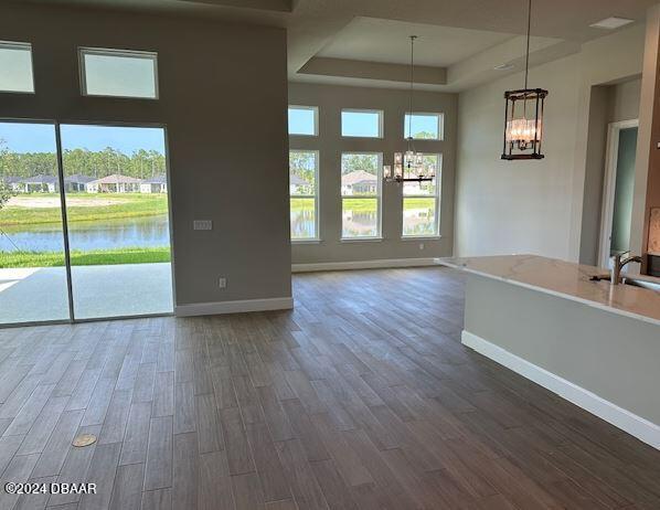 interior space featuring a tray ceiling, a water view, dark hardwood / wood-style flooring, and a notable chandelier