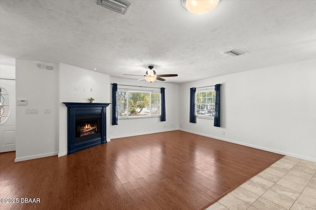 unfurnished living room with visible vents, a warm lit fireplace, a textured ceiling, and wood finished floors