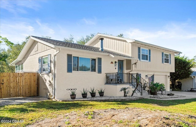 split level home featuring brick siding, a front lawn, fence, a garage, and driveway