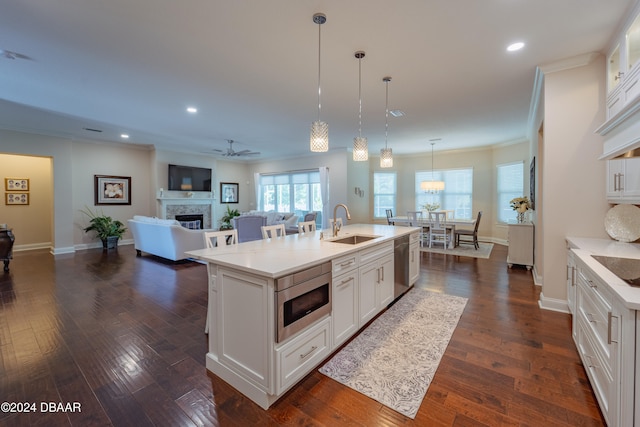 kitchen with white cabinetry, dark wood-type flooring, stainless steel appliances, an island with sink, and decorative light fixtures