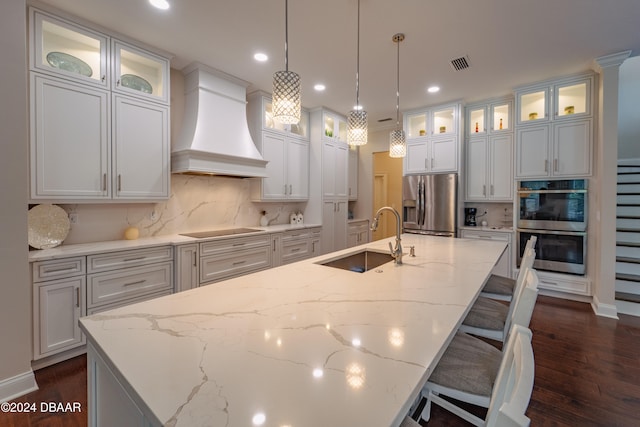 kitchen featuring sink, an island with sink, decorative light fixtures, appliances with stainless steel finishes, and custom exhaust hood