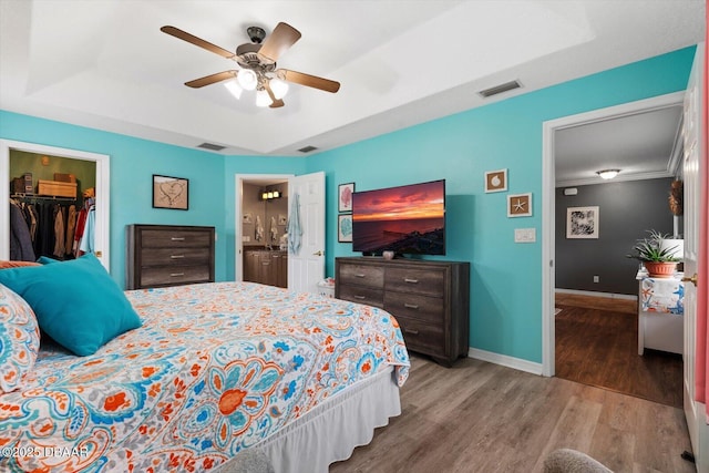 bedroom featuring ensuite bath, a walk in closet, a closet, ceiling fan, and a tray ceiling