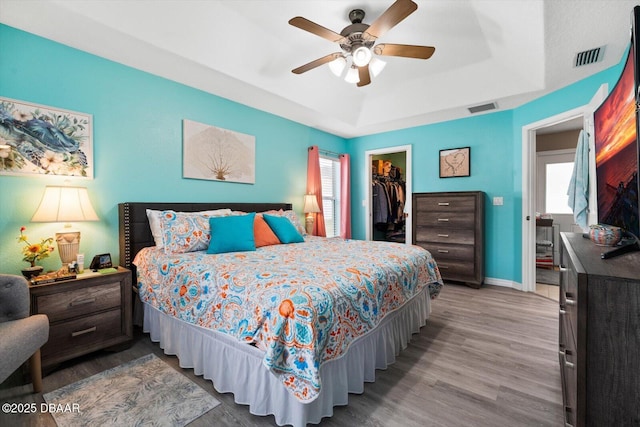 bedroom with a walk in closet, wood-type flooring, a closet, a raised ceiling, and ceiling fan