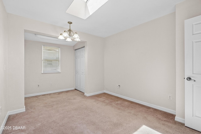 carpeted spare room featuring a chandelier, a skylight, and baseboards