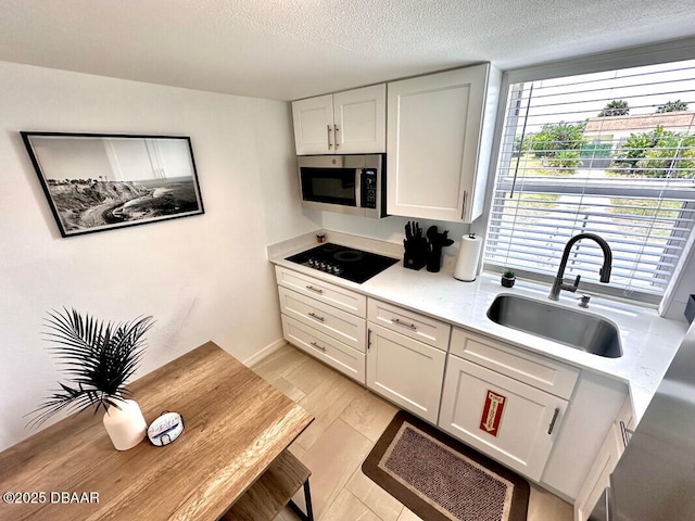 kitchen featuring stainless steel microwave, light countertops, a textured ceiling, black electric cooktop, and a sink