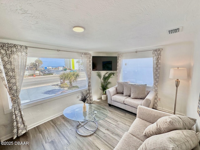 living room featuring visible vents, a textured ceiling, baseboards, and wood finished floors