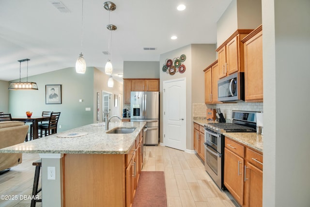kitchen with hanging light fixtures, appliances with stainless steel finishes, sink, tasteful backsplash, and an island with sink