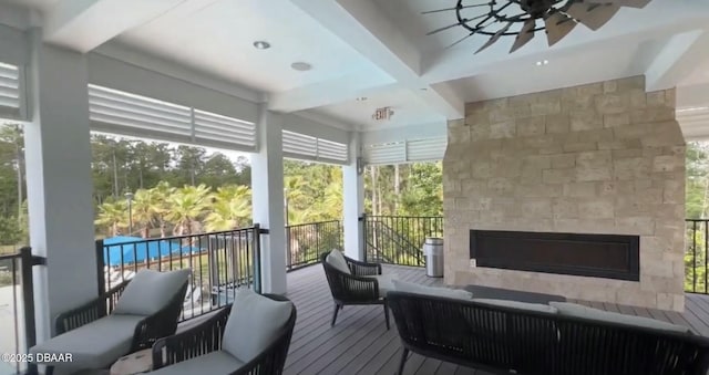 sunroom with ceiling fan, beamed ceiling, and a fireplace