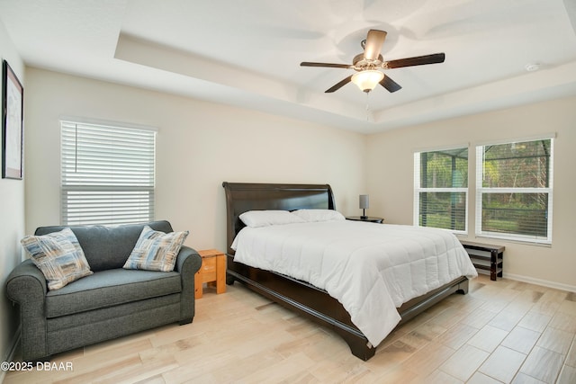 bedroom featuring ceiling fan, multiple windows, and a tray ceiling