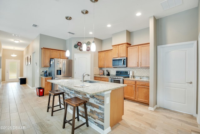 kitchen with hanging light fixtures, sink, light stone countertops, an island with sink, and stainless steel appliances