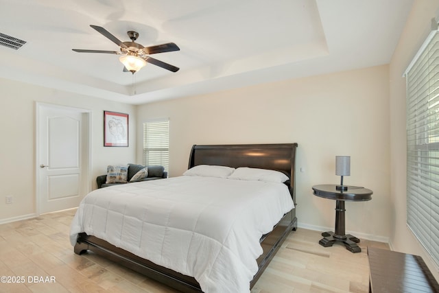 bedroom featuring ceiling fan, light hardwood / wood-style floors, and a tray ceiling