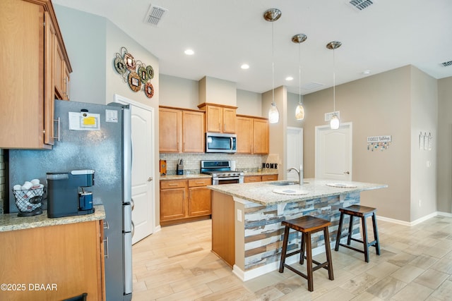 kitchen with appliances with stainless steel finishes, sink, hanging light fixtures, light stone counters, and a center island with sink
