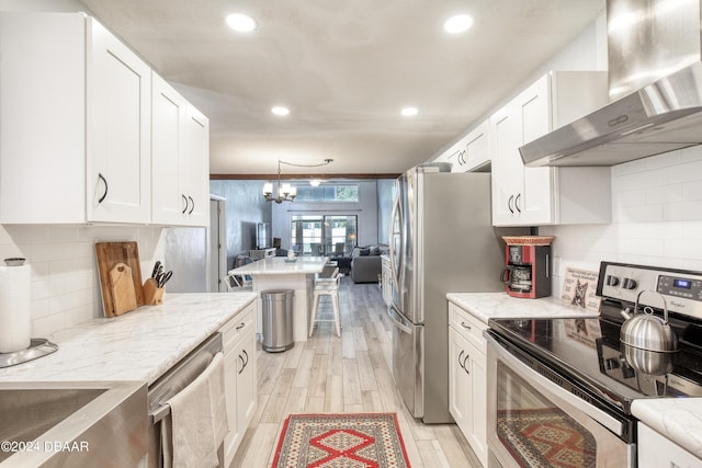 kitchen with white cabinets, appliances with stainless steel finishes, a chandelier, and wall chimney exhaust hood