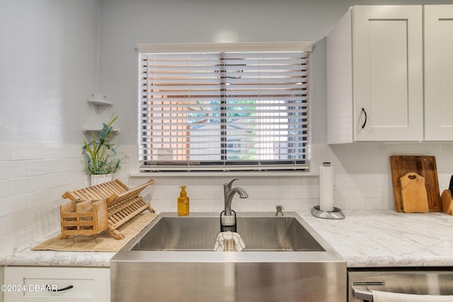 kitchen with decorative backsplash, white cabinetry, stainless steel dishwasher, and sink