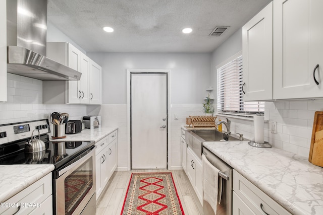 kitchen with white cabinets, wall chimney range hood, a textured ceiling, and appliances with stainless steel finishes