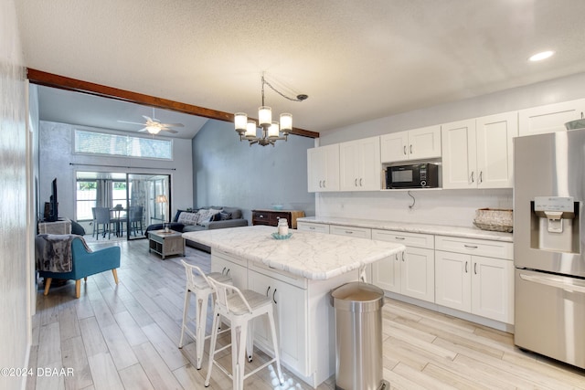 kitchen featuring stainless steel refrigerator with ice dispenser, ceiling fan with notable chandelier, a center island, white cabinetry, and hanging light fixtures