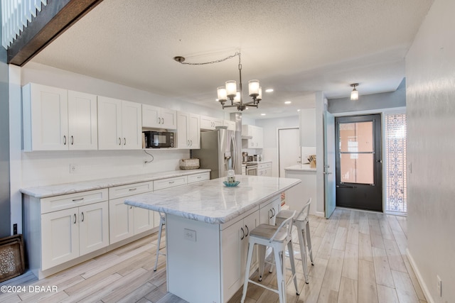 kitchen with stainless steel fridge, decorative light fixtures, white cabinets, light hardwood / wood-style floors, and a breakfast bar area