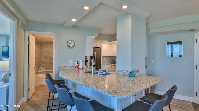 2625 S Atlantic Ave Unit 18Sw, Daytona Beach, FL 32118 - kitchen featuring kitchen peninsula, light wood-type flooring, sink, white cabinetry, and a breakfast bar area