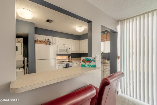 kitchen featuring kitchen peninsula, a kitchen breakfast bar, white appliances, stacked washing maching and dryer, and white cabinets