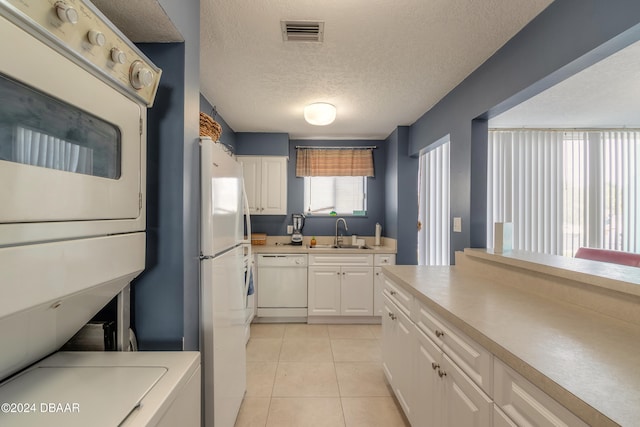 kitchen with a textured ceiling, sink, white cabinetry, stacked washer and dryer, and white appliances