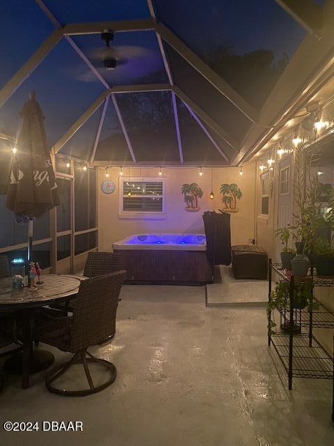 patio at night with glass enclosure and an outdoor hot tub