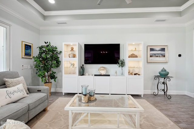 living room with hardwood / wood-style floors, crown molding, a raised ceiling, and built in shelves