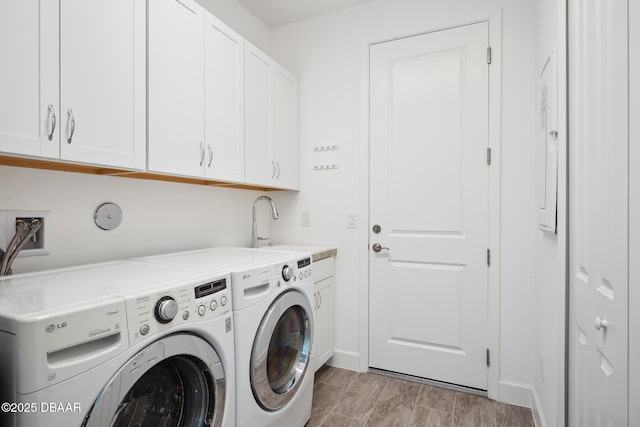 clothes washing area featuring cabinets, washing machine and clothes dryer, and light hardwood / wood-style flooring