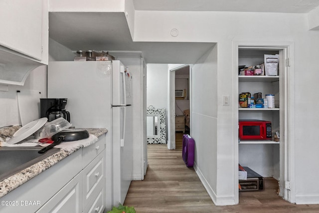 kitchen with white refrigerator, light hardwood / wood-style floors, and white cabinets