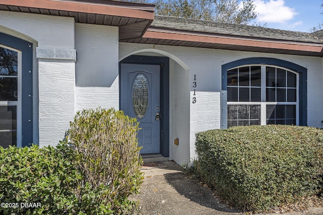 doorway to property with a shingled roof and stucco siding