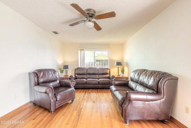 living room with ceiling fan, light wood-type flooring, and a textured ceiling