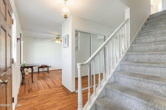 stairs with hardwood / wood-style flooring and ceiling fan