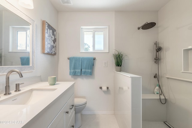 bathroom with toilet, plenty of natural light, vanity, and tiled shower