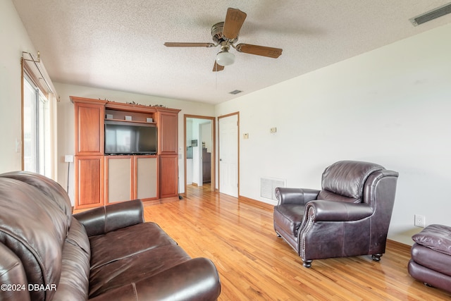 living room featuring ceiling fan, light hardwood / wood-style flooring, and a textured ceiling